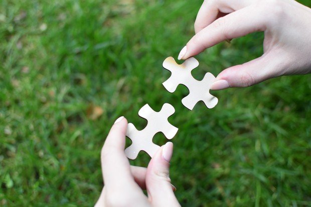 Zwei weiße Puzzleteile werden von zwei Händen aneinandergefügt.