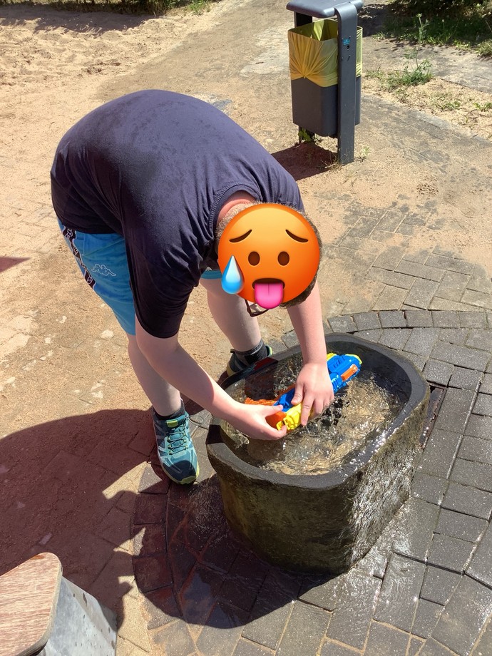 Schüler, der eine Wasserspritze am Brunnen nachfüllt.