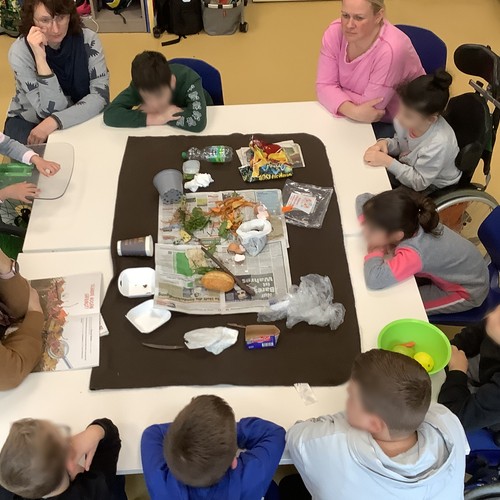 Kinder sitzen um einen Tisch auf dem verschiedene Sorten Abfall liegen.