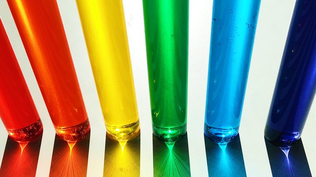 Sechs Wassersäulen in Regenbogenfarben stehen nebeneinander. Sie werden von hinten beleuchtet und werfen bunte Schatten.