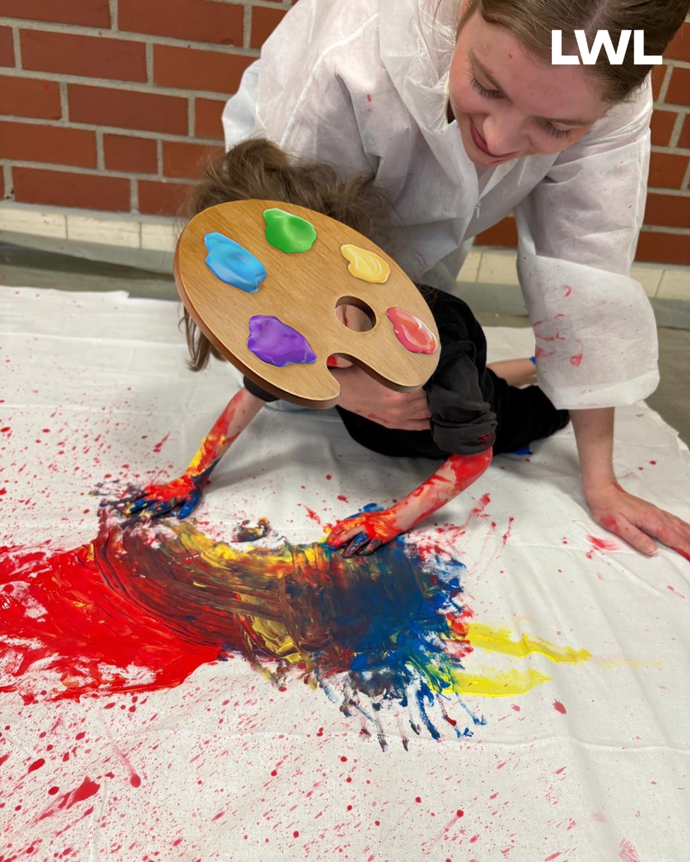 Eine Schülerin malt auf ein riesiges weißes Tuch auf dem Boden.