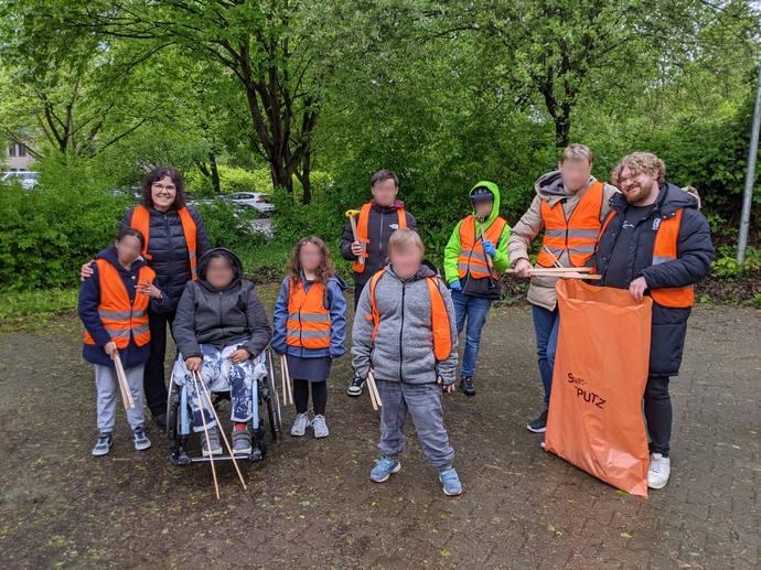 Ein Gruppenbild von Schülerinnen und Schülern mit Warnwesten, Greifzangen und Müllbeuteln.