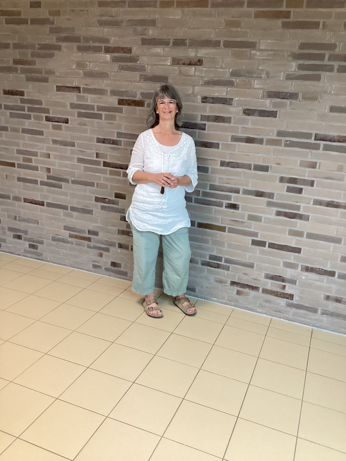 Frau Krause steht lächelnd vor einer Kachelwand.