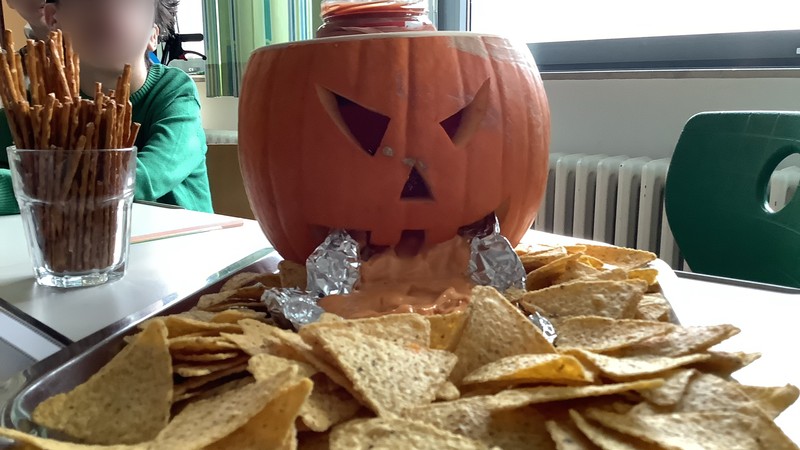Ein Kürbis, in den ein Gesicht geschnitzt ist, spuckt Käsesoße und Nachos aus.