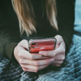 Ein junges Mädchen hält ein rot-silbernes Smartphone in der Hand.