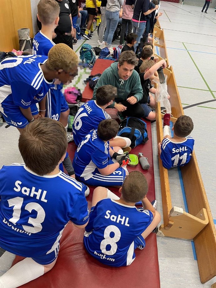 die Schüler und Schülerinnen sitzen am Spielfeldrand und besprechen sich mit dem Trainer.