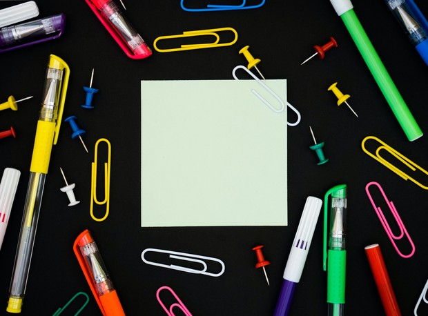 Notizzettel, viele Stifte und Büroklammern liegen auf einer Schreibtisch-Unterlage