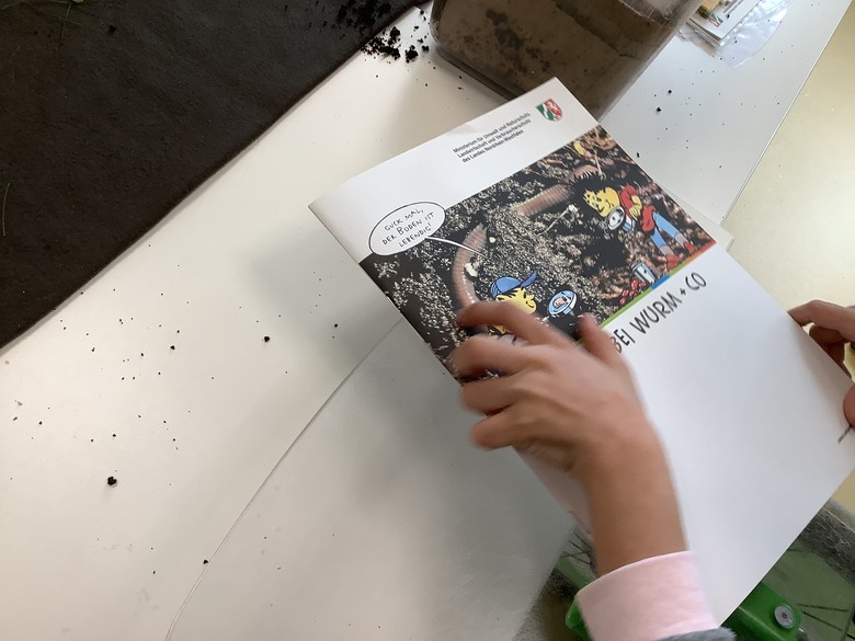 Eine Kinderhand hält eine Informationsbroschüre zum Thema Kompost.
