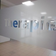 Schriftzug "Therapie" an der Glastür zum Therapie-Flur: das Glas ist matt, die Buchstaben sind durchsichtig.