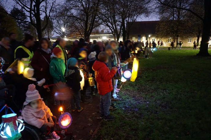Viele Personen, vor allem Kinder, stehen im Dunkeln an einer Wiese und halten leuchtende St.-Martins-Laternen