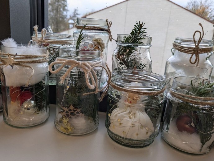 mehrere leere Marmeladengläser gefüllt mit Tannengrün, Engelsfiguren und Weihnachtskugeln