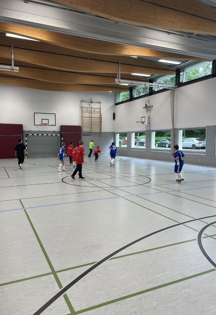 Eine Spielszene. Schülerinnen und Schüler sind auf dem Spielfeld in der Turnhalle zu sehen.