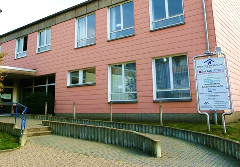 Haus der Begegung in Bochum. Ein rotes Gebäude mit 5 Fenstern im OG und drei Fenstern im Erdgeschoss. Eine Rampe führt zur EIngangstür.