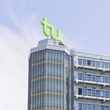 Die oberen Stockwerke eines Gebäudes der TU Dortmund: ein Turm auf gleicher Höhe mit einem sich direkt daran anschließenden Flachdachbau. Auf dem Dach des Turms sind die grünen Buchstaben "TU"