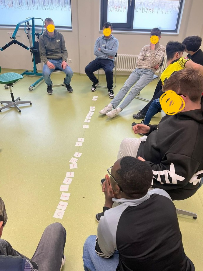Schüler sitzen im Stuhlkreis. Auf dem Boden liegen Karten.