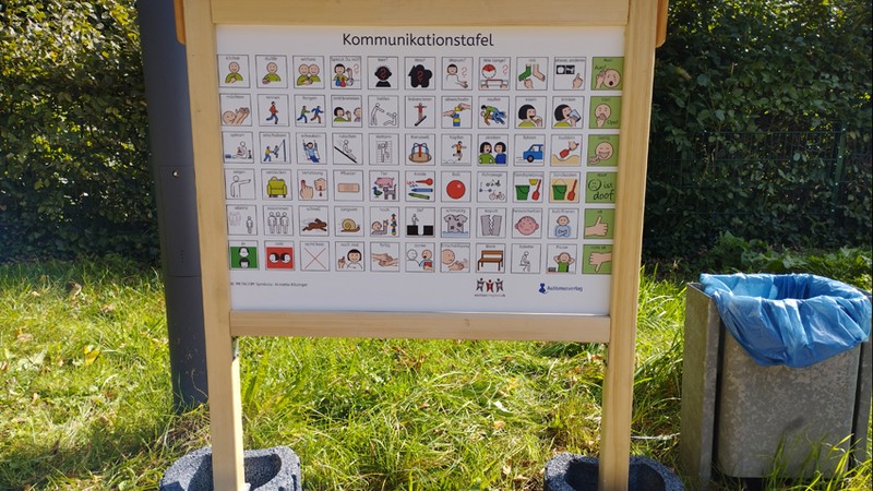 Eine Kommunikationstafel steht am Schulhofrand. Darauf 6 mal 11 Metacomsymbole