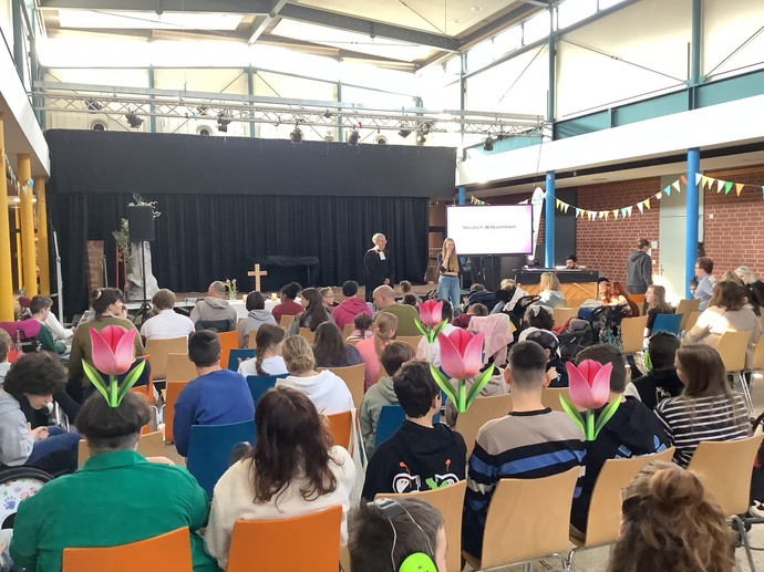 Ostergottesdienst: Ein Pfarrer steht vor der Bühne und das Forum ist gefüllt mit SchülerInnen.