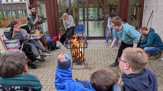 Personen stehen und sitzen im Kreis um einen Feuerkorb.