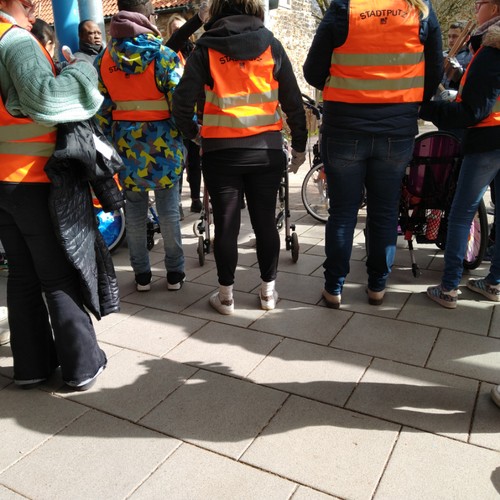 mehrere Personen mit orangenen Warnwesten von hinten zu sehen stehen nebeneinander.
