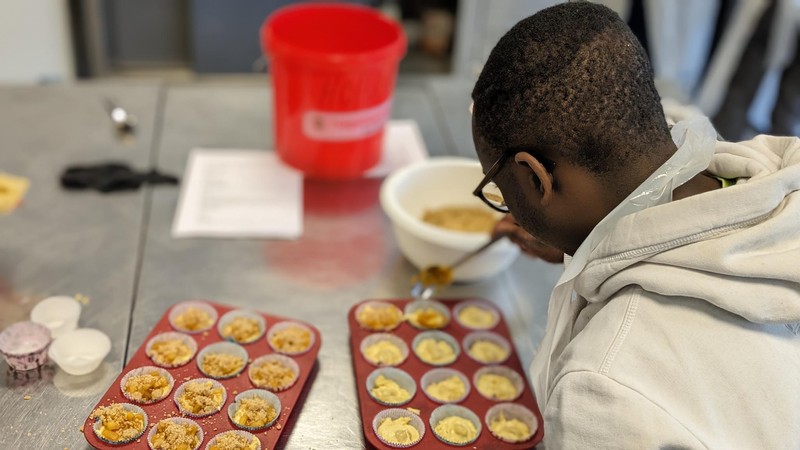 Ein Schüler füllt Teig in Muffinförmchen