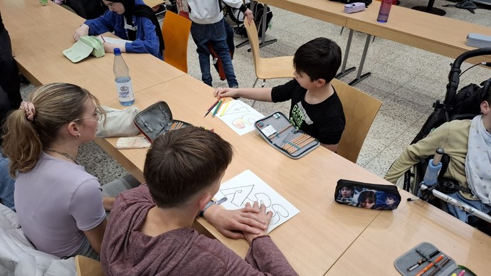 SchülerInnen sitzen am Tisch und zeichnen Klassenschilder.
