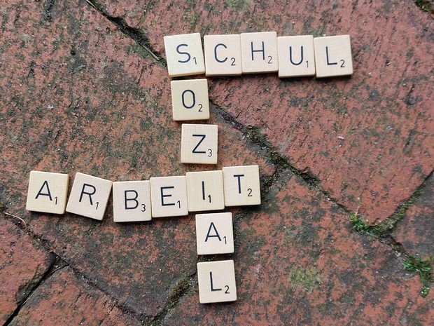 Scrabble-Steine auf roten Pflastersteinen bilden die Wörter Schul - Sozial - Arbeit
