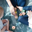 Zwei Kleinkinder im frühen Kindergartenalter sitzen zusammen mit einer erwachsenen Person auf dem Boden und spielen mit Holzwürfeln, auf denen Buchstaben aufgedruckt sind.