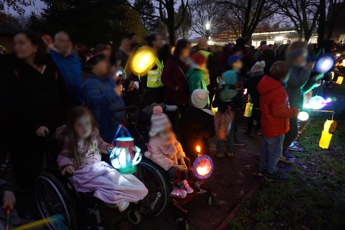 Viele Personen, vor allem Kinder, stehen im Dunkeln an einer Wiese und halten leuchtende St.-Martins-Laternen