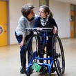 EIne Frau steht neben einem Mädchen in einem Stehtrainer. Beide lächeln sich an.