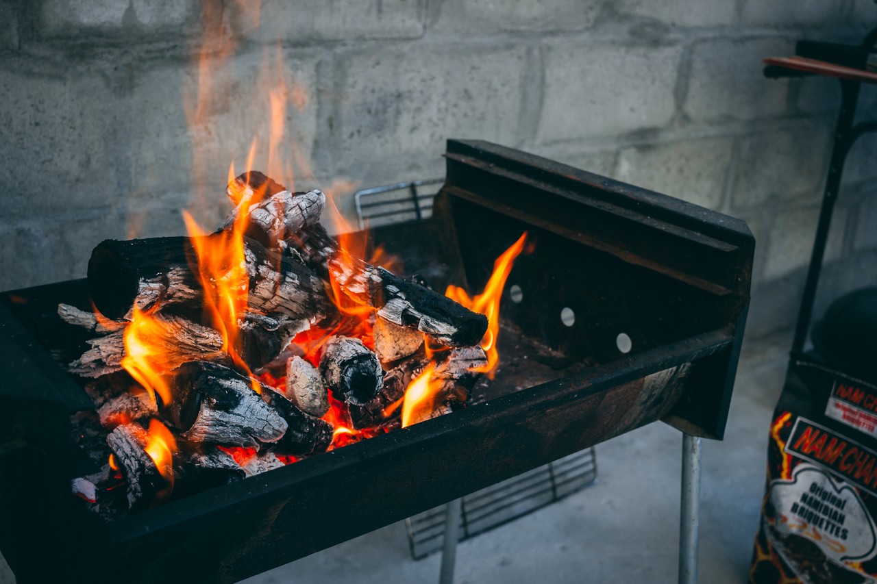 Ein Grill vor einer Mauer. Aus den glühenden Kohlen schlagen Flammen.