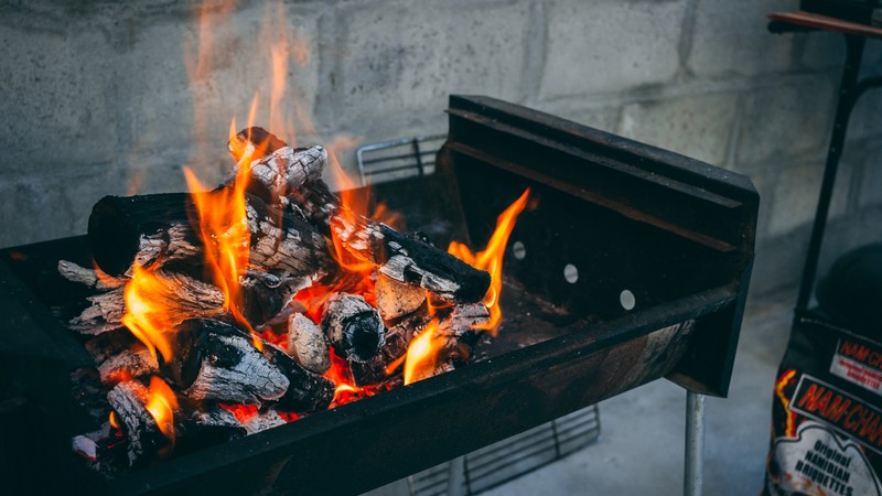 Ein Kohlegrilll mit Weißglut aus der Falmmen züngeln steht vor einer Mauer.