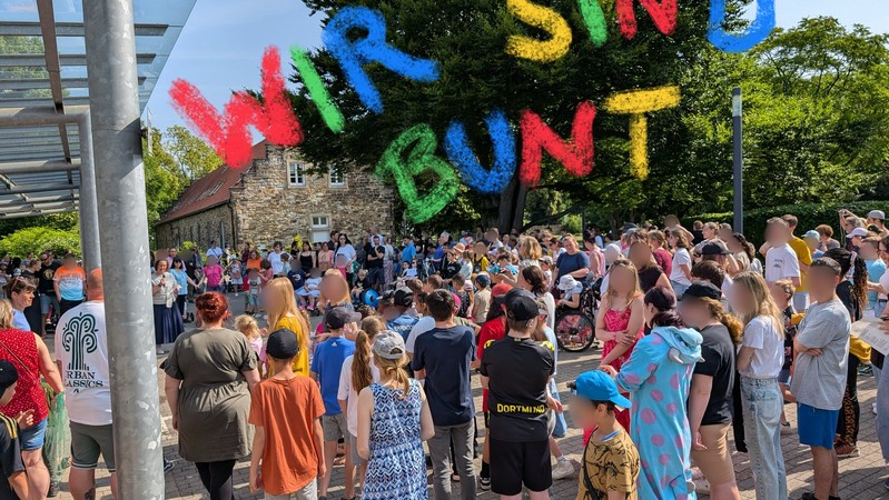 Eine große Gruppe Menschen steht im Kreis. Wir sind bunt