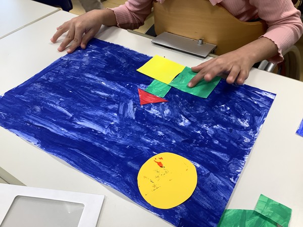 Ein Kind legt bunte geometrische Formen auf ein blau angemaltes Papier.