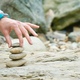 Eine Hand, die vier flache Steine zu einem Turm aufschichtet.