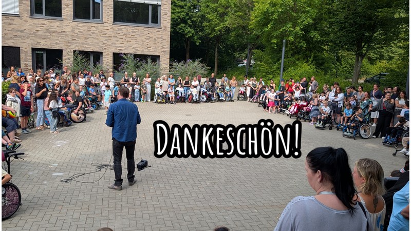 Ein Kreis von vielen menschen auf Schulhof 1. In der Mitte steht Herr Ebel mit einem Mikrophon
