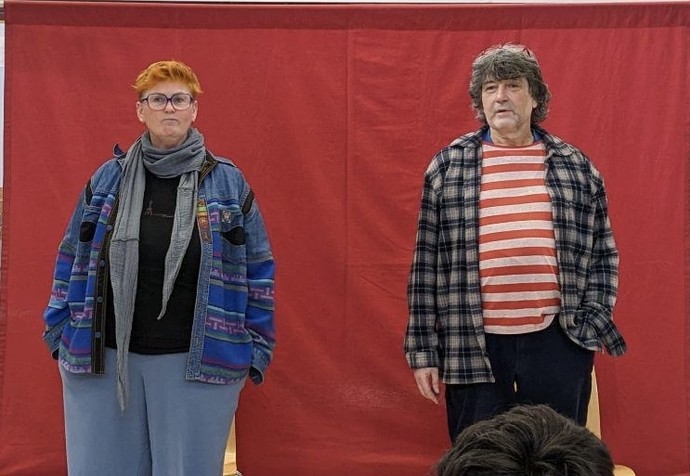 Ein Frau und ein Mann stehen vor einem roten Hintergrund auf der Bühne.