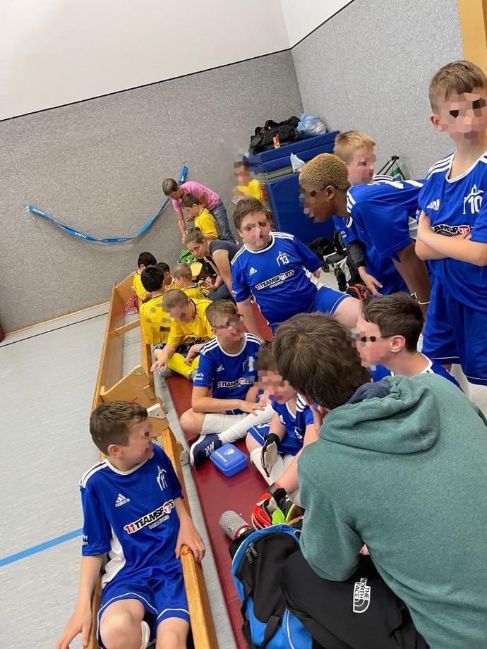 die Schüler und Schülerinnen sitzen am Spielfeldrand und besprechen sich mit dem Trainer.