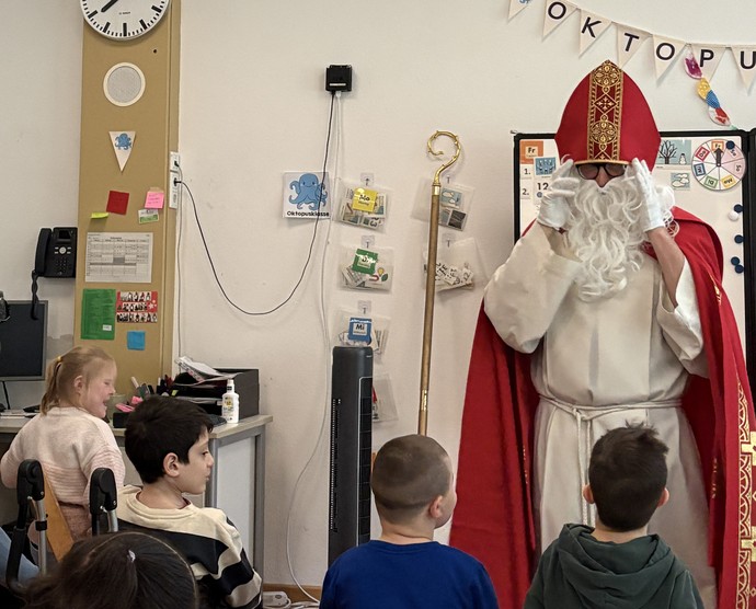 Der Nikolaus ist steht vor einer Reihe sitzender Schülerinnen und Schüler.