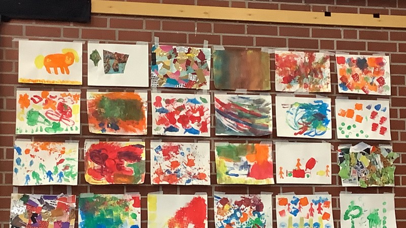 Fertige Kunstwerke, die an einer roten Steinwand hängen. Die Kunstwerke sind bunt und mit verschiedenen Techniken gestaltet.