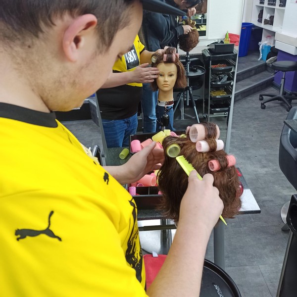Schüler frisiert einen Puppenkopf.